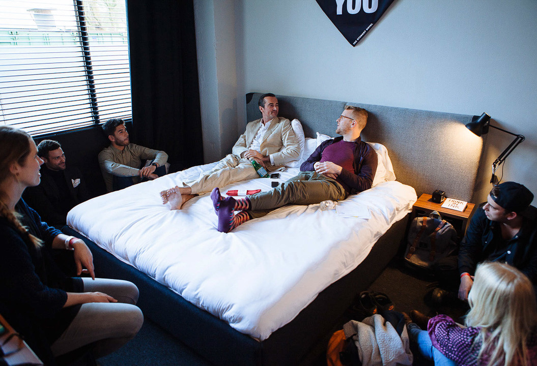 Speakers sit on bed surrounded by an audience in a guest room for an event at The Student Hotel 