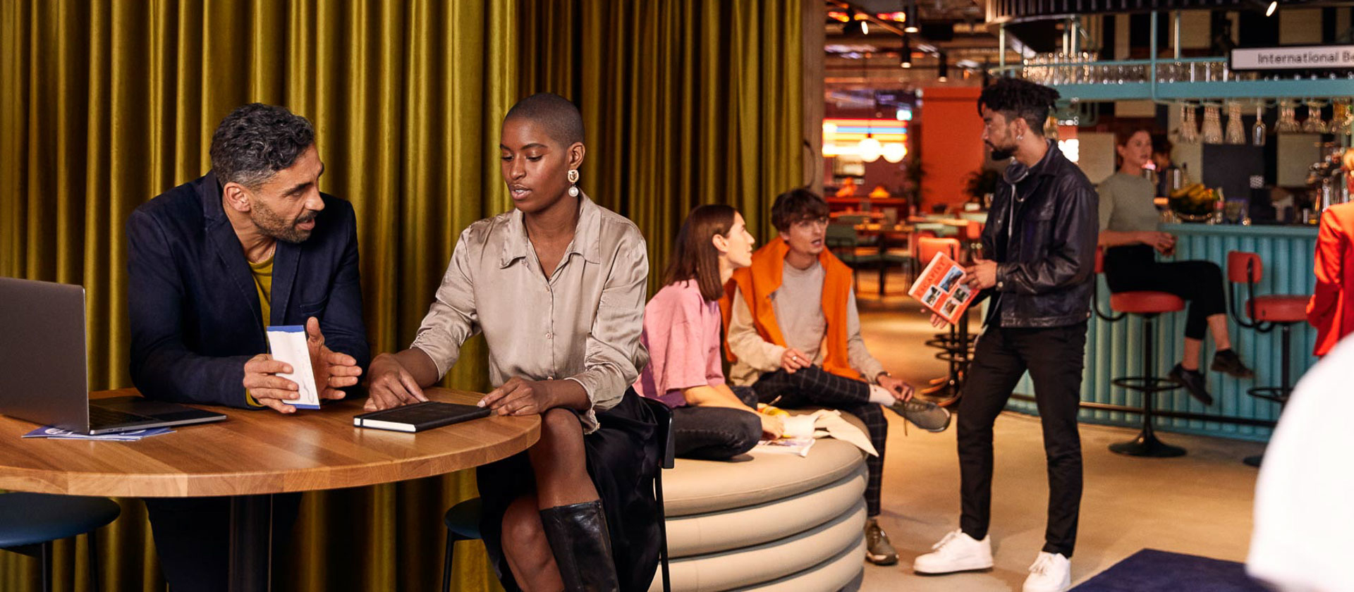 Group sits on bar table near an event and restaurant space at The Student Hotel Bologna