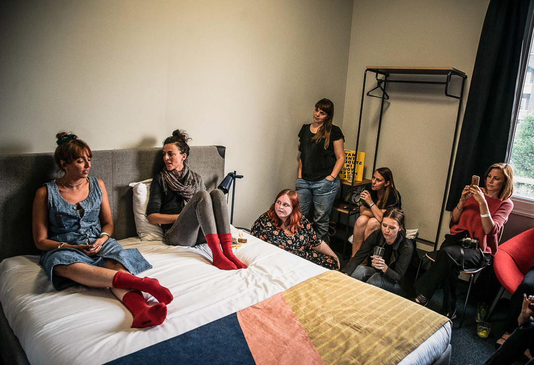 Speakers sit on bed surrounded by an audience in a guest room for an event at The Student Hotel Paris